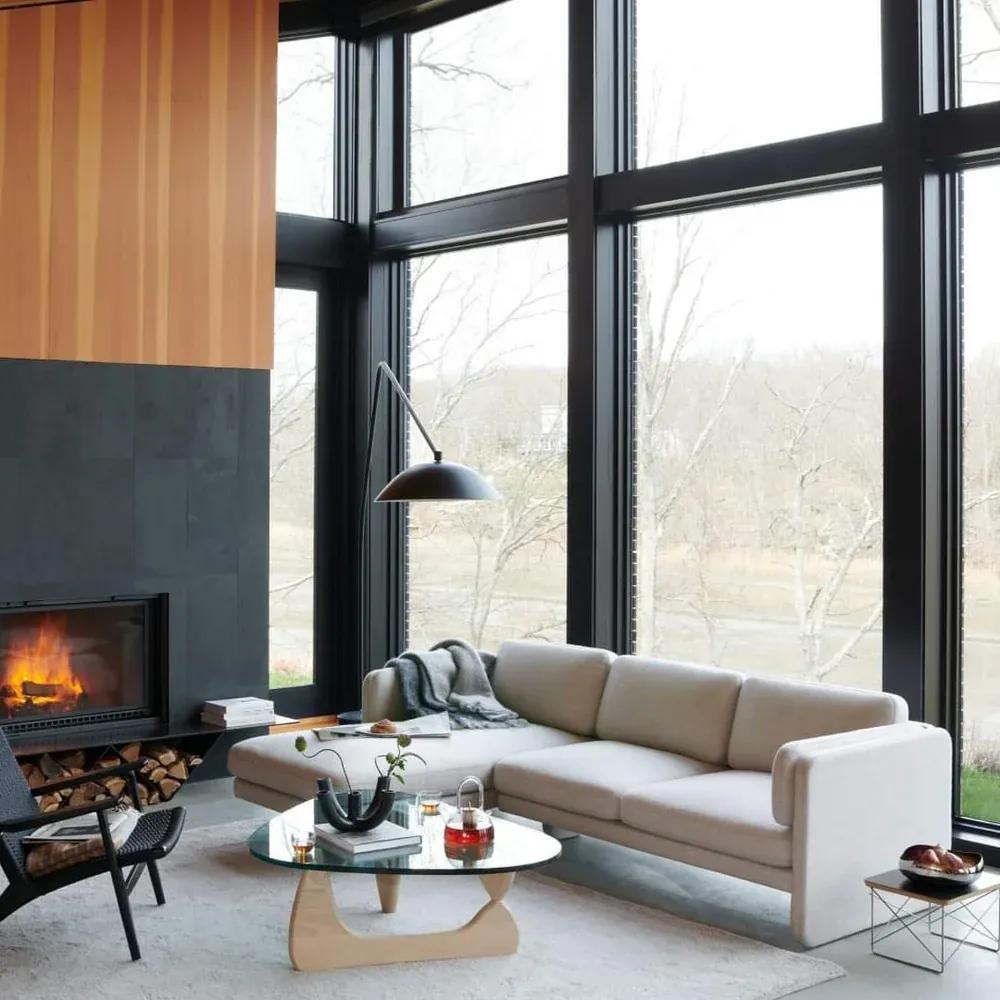 The three-seat sofa in front of floor-to-ceiling windows next to a fireplace