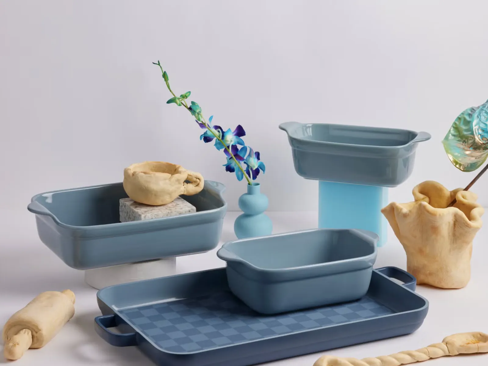 Our Place bakeware set in blue: two square bakers, a loaf pan and a sheet pan, styled with bread dough