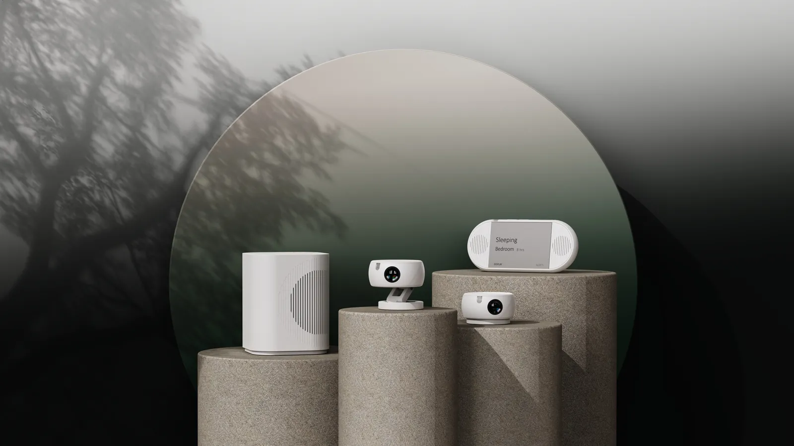 The LumiMate hub, two sensor units and the caregiver display on stone plinths in front of a large round mirror reflecting a tree