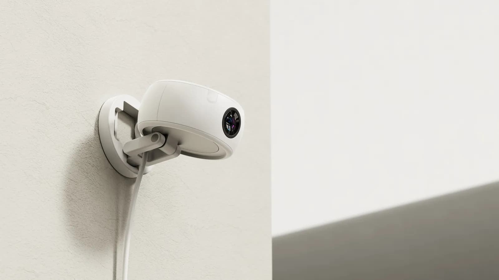 The sensor unit mounted on a textured white wall, its stand folded flat against the wall plate and the cord running down