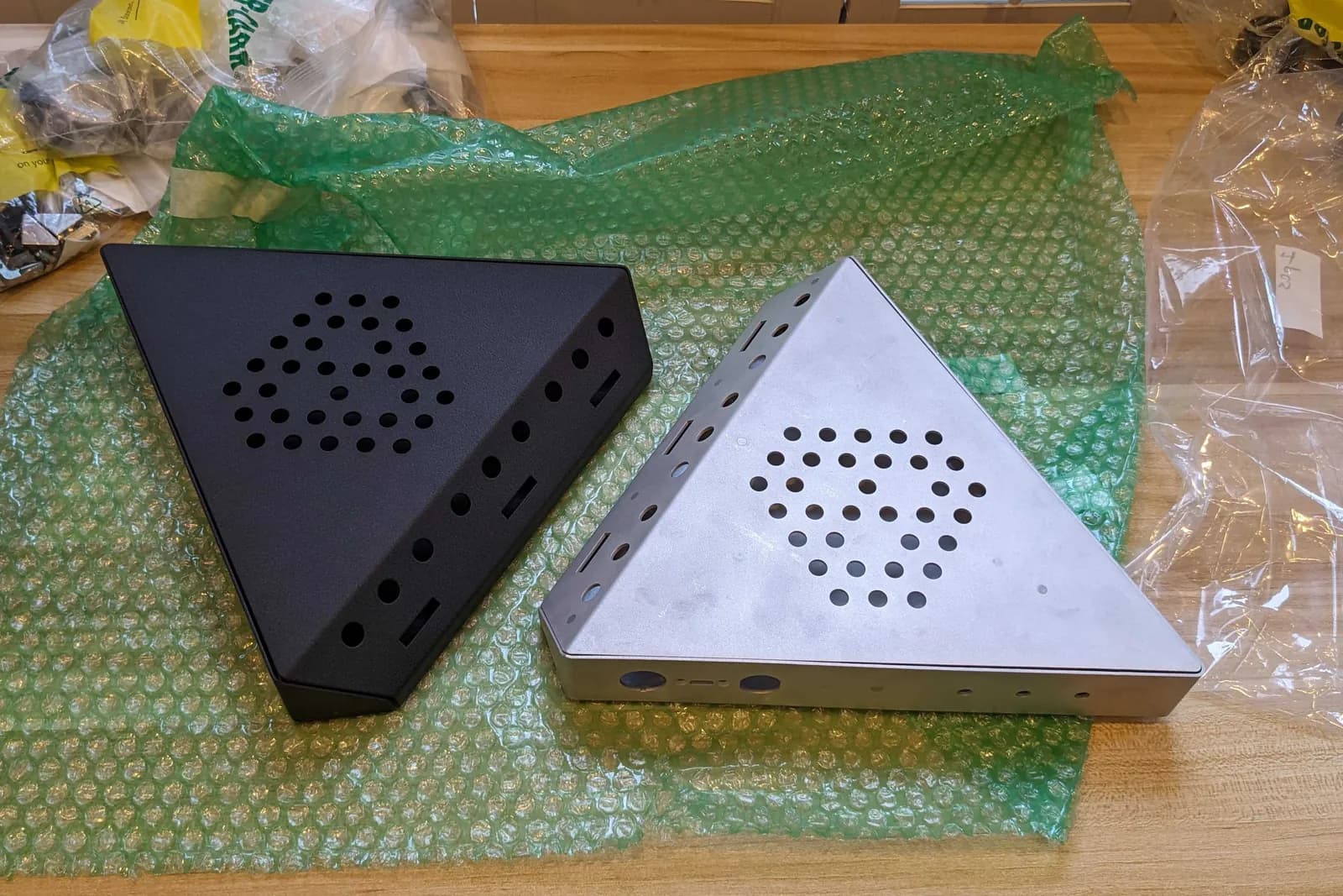 Two bent enclosures in bubble wrap, one powder-coated black and one raw aluminium