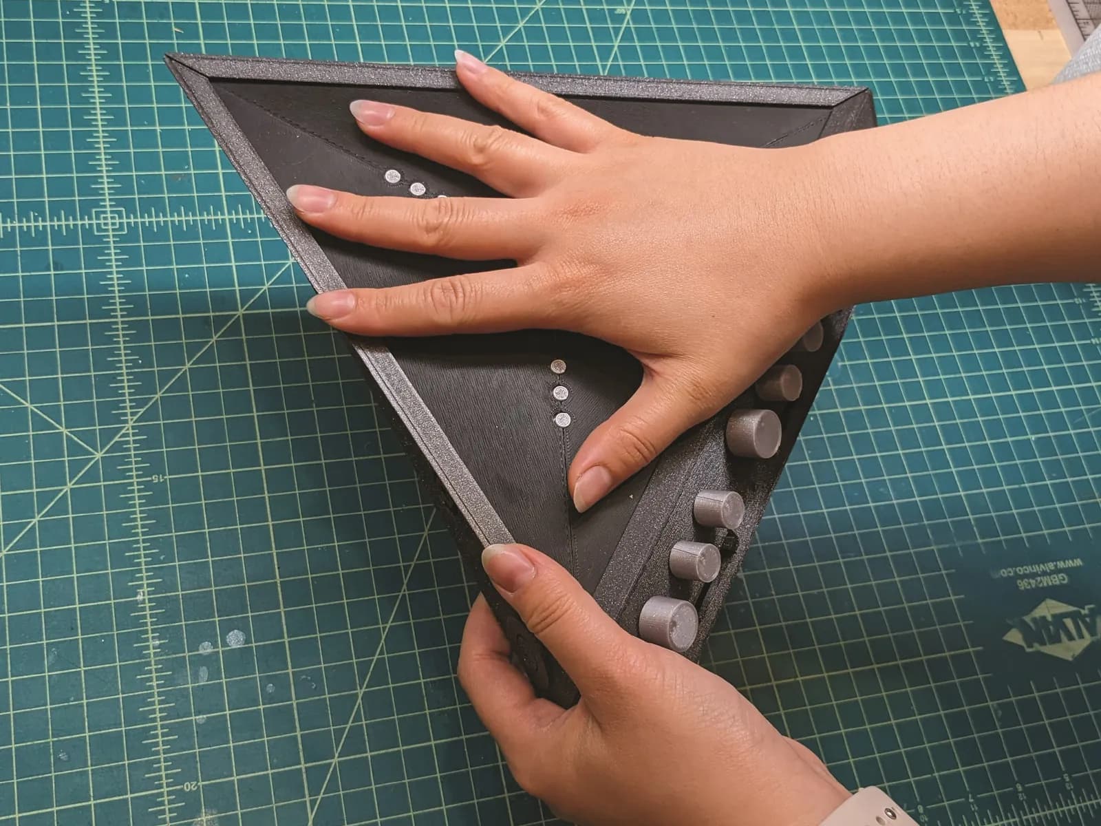 A hand resting on a 3D printed prototype on a cutting mat