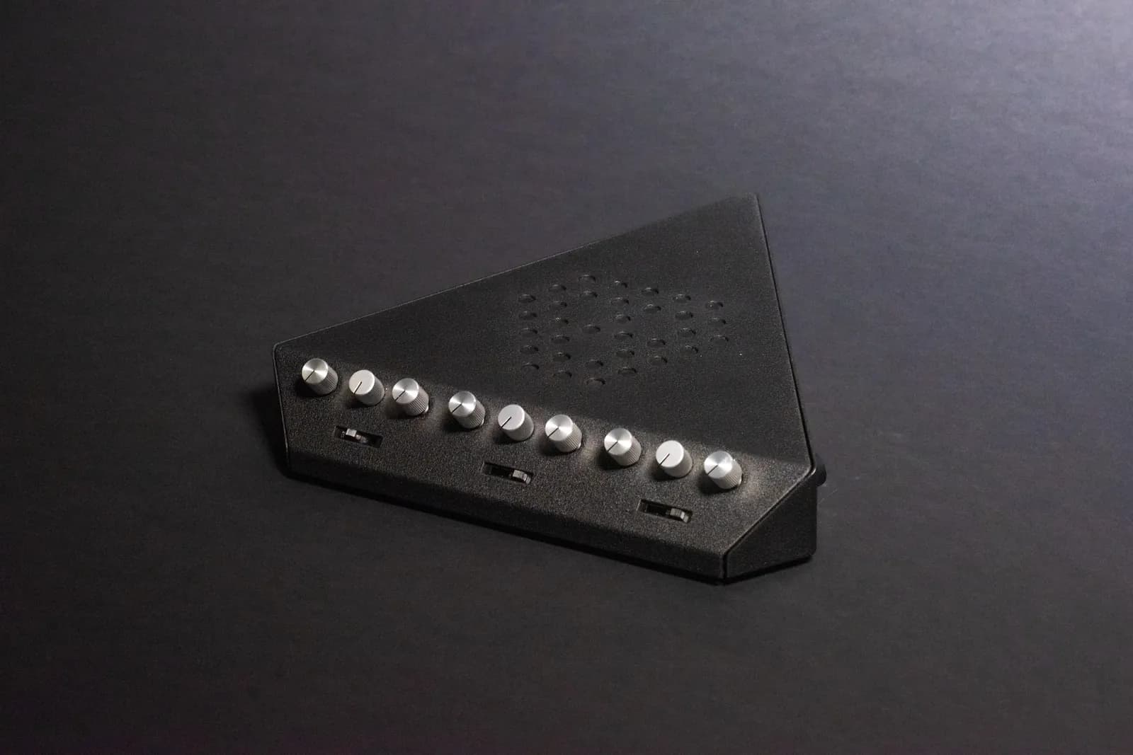 Assembled sheet metal prototype on black: silver knobs along the front edge and the perforated triangle on top