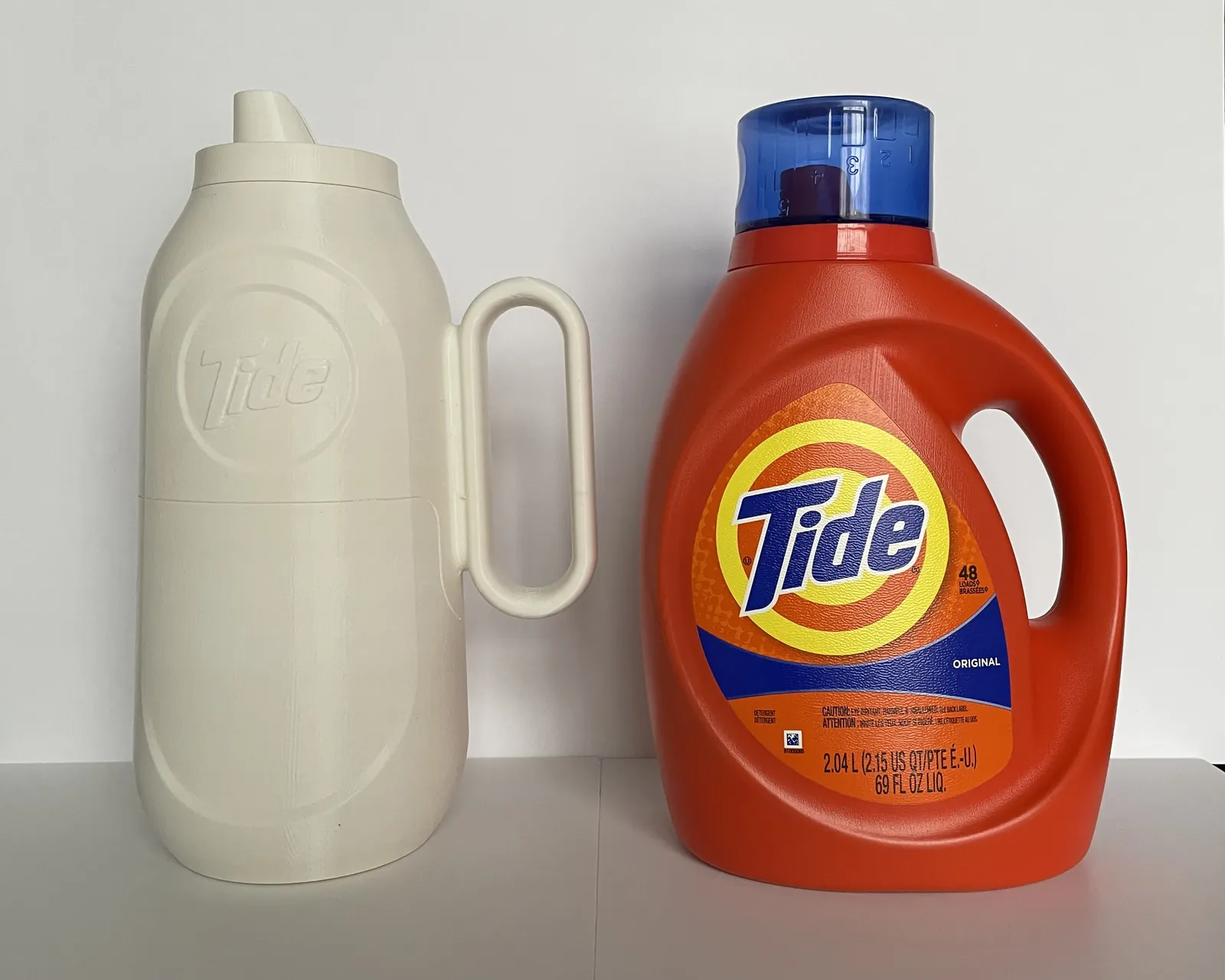 3D print of the spouted bottle with a round handle next to the current Tide bottle