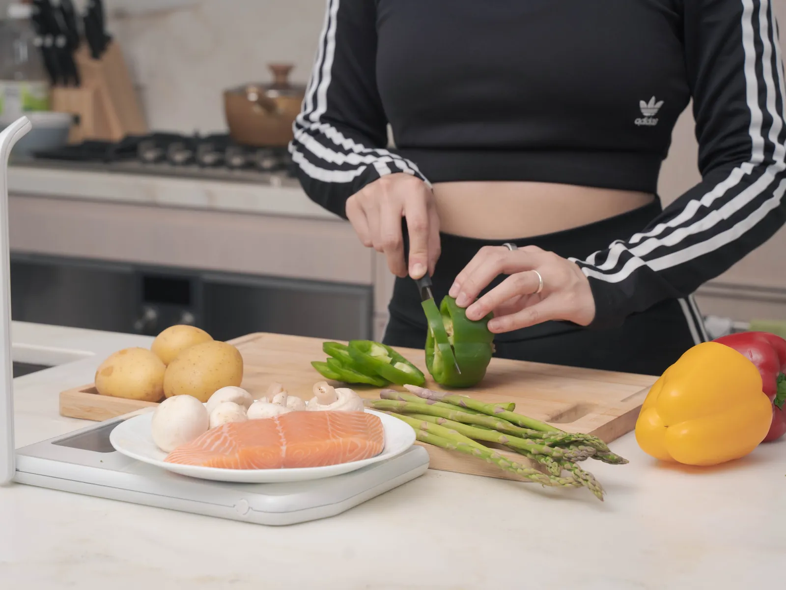 A person chopping peppers at a kitchen counter with a salmon fillet on the scale beside the cutting board