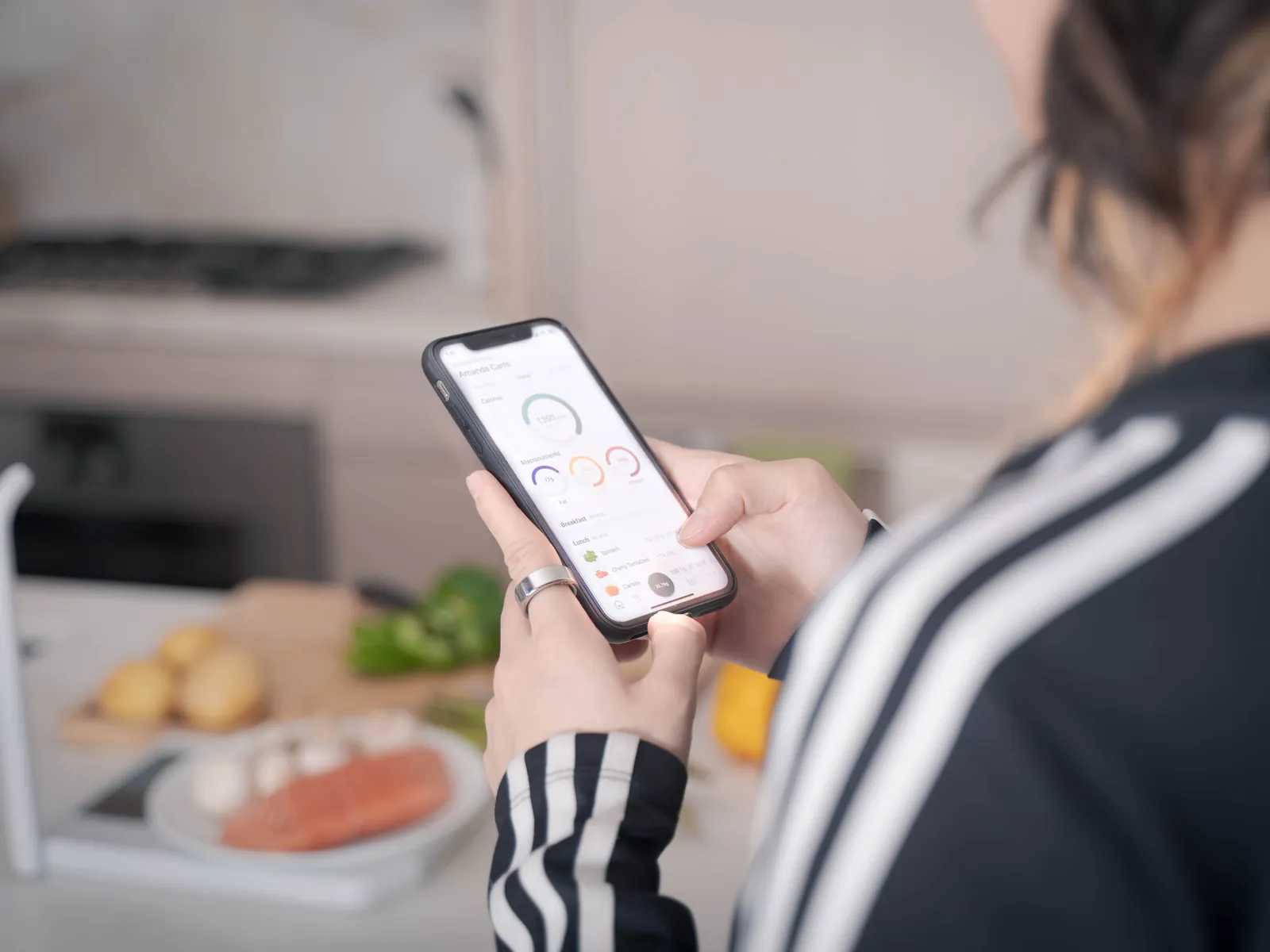 Over-the-shoulder view of a person checking the Nutri dashboard on their phone, the scale with salmon on it on the counter behind