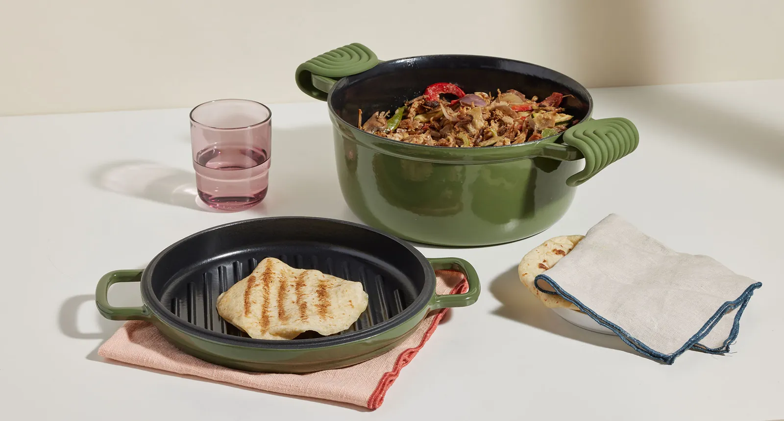 Green cast iron Perfect Pot full of food next to a round cast iron grill with flatbread