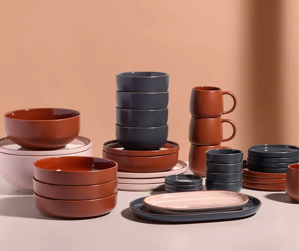 Stacks of terracotta, charcoal, and pink bowls, plates, and mugs
