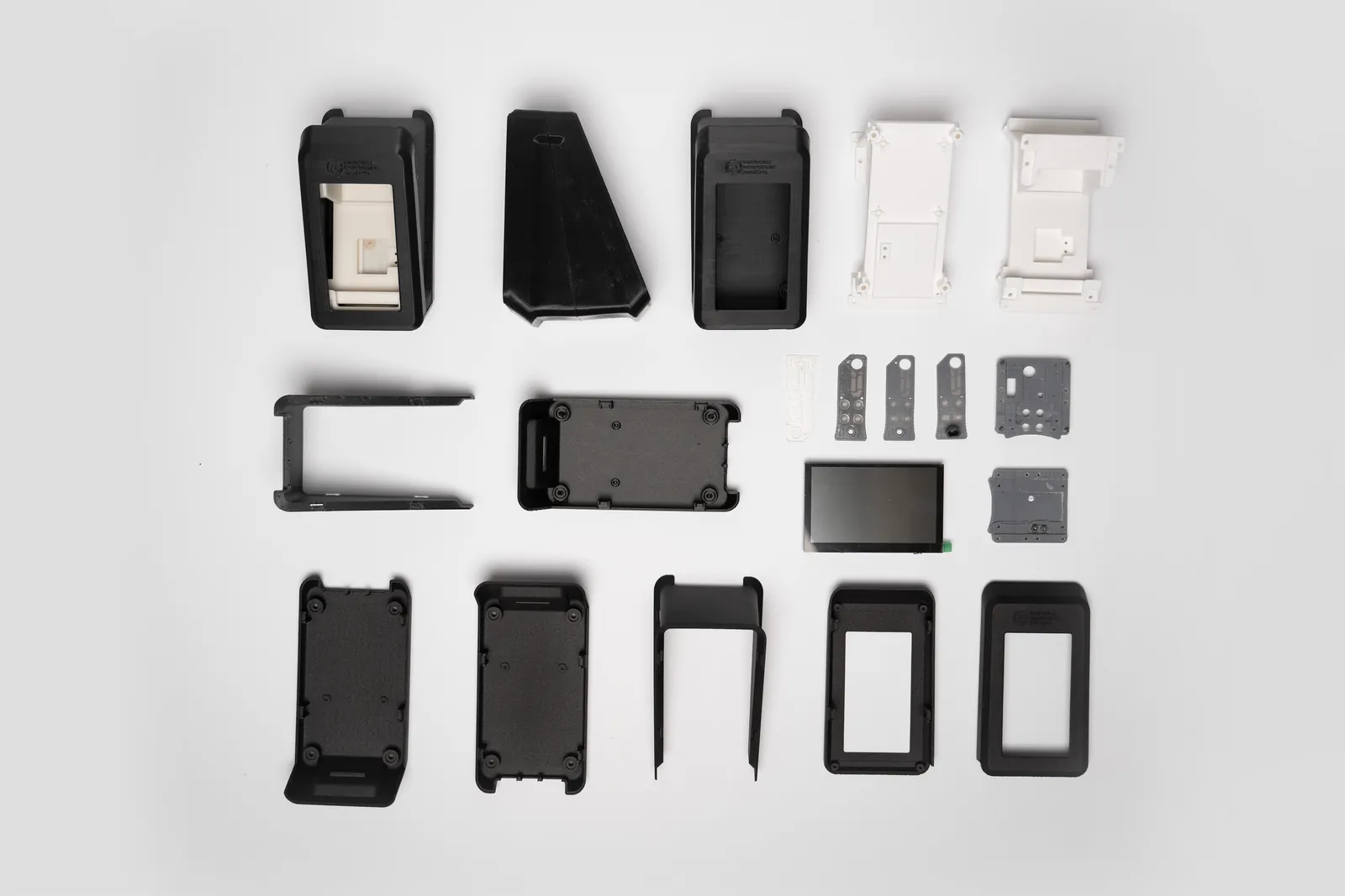 Flat lay of the 3D-printed enclosure parts, brackets, screen and PCB from the pilot build on a white surface