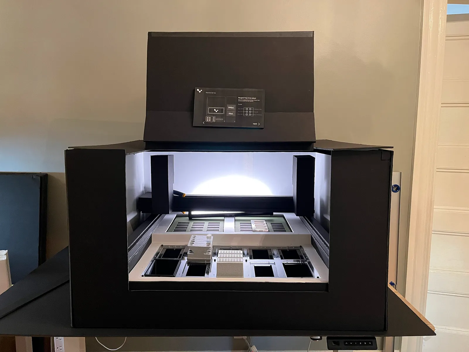 Black foam core prototype of the instrument with the door folded up, a screen mock-up on the door and labware on the bed