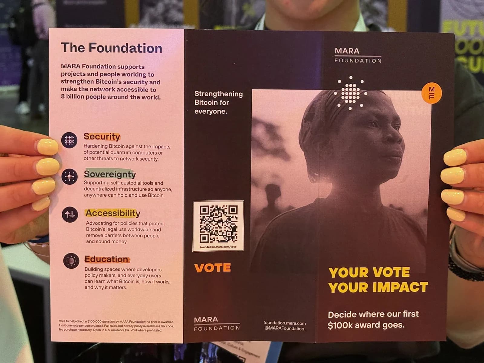 The Foundation brochure held open: The Foundation panel with security, sovereignty, accessibility and education, a vote QR code, and Your vote your impact
